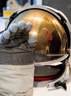 Photo of a glove and a space helmet with Sonny Reihm's face reflected in visor