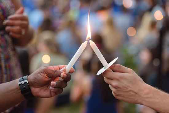 image of the hand of an African-American person and a white person lighting candles.